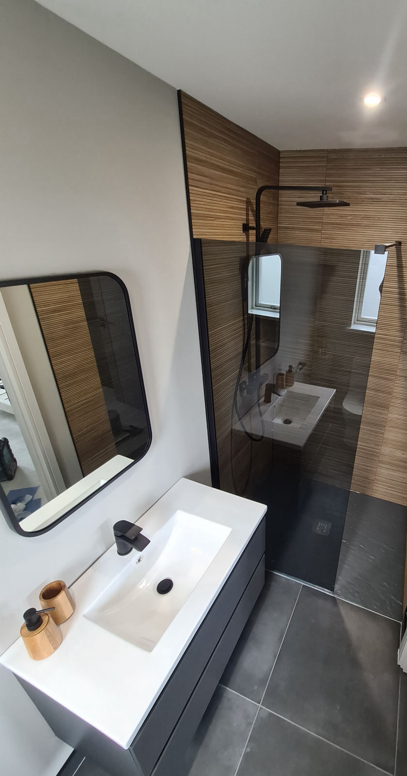A shower room in wood-effect ribbed tile with a black framed screen and a slate floor