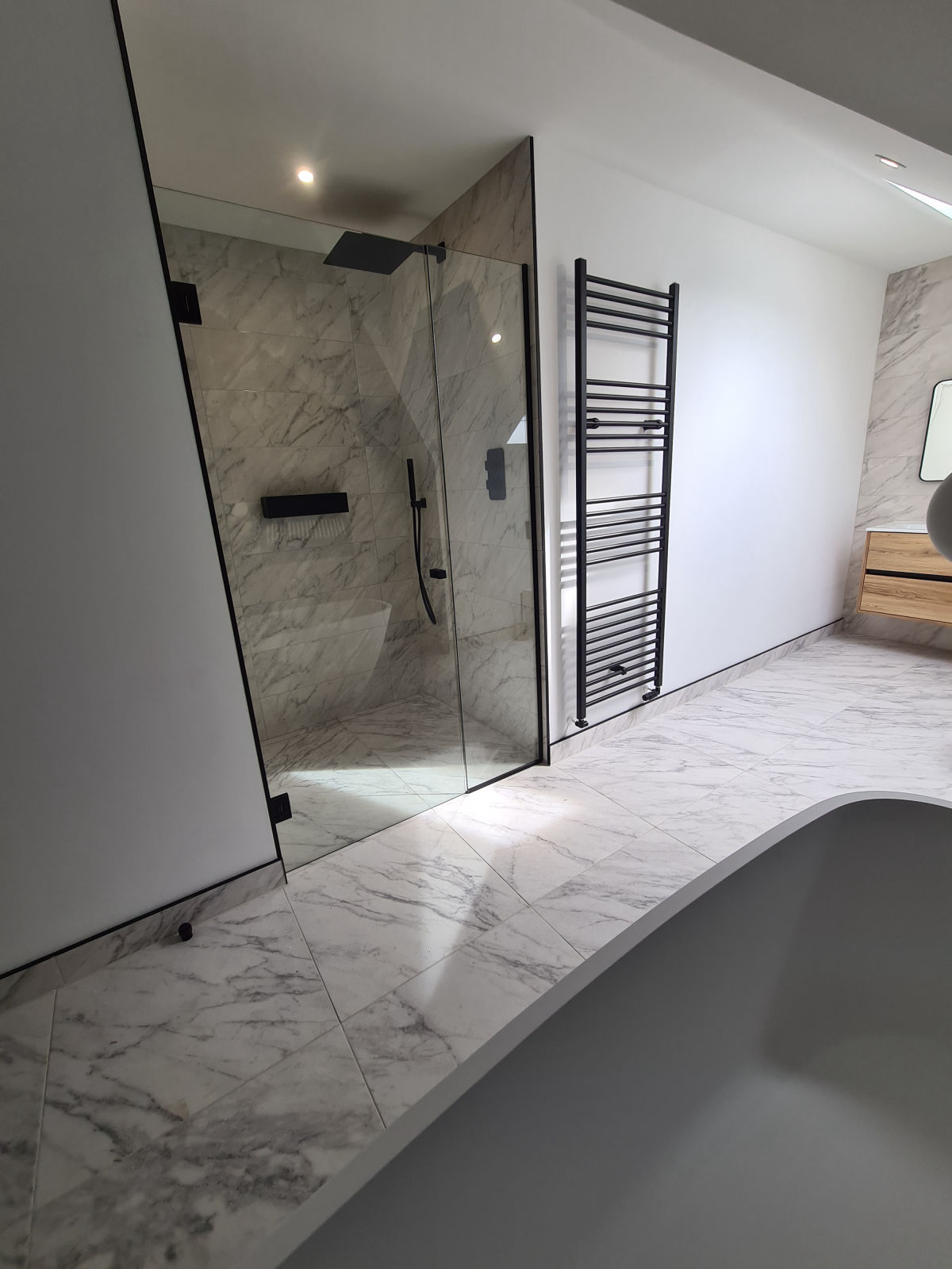 A walk-in shower with a black frameless screen and a grey freestanding bath in the foreground